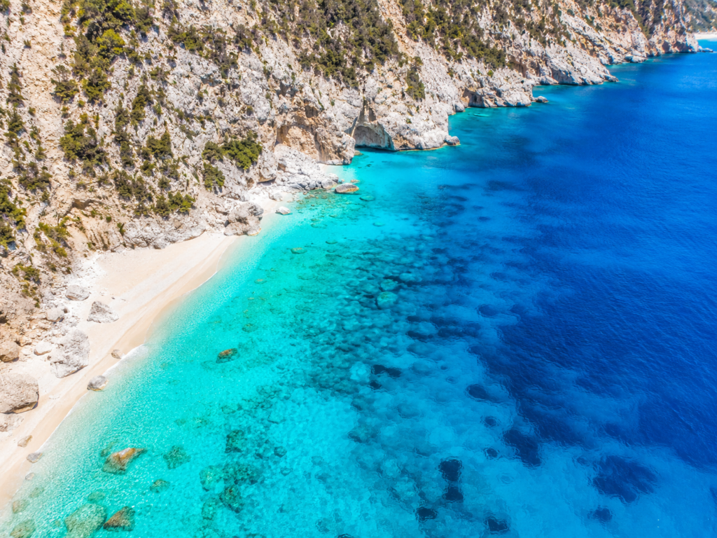 Aerial view of a pristine Mediterranean coastline with clear turquoise water and limestone cliffs