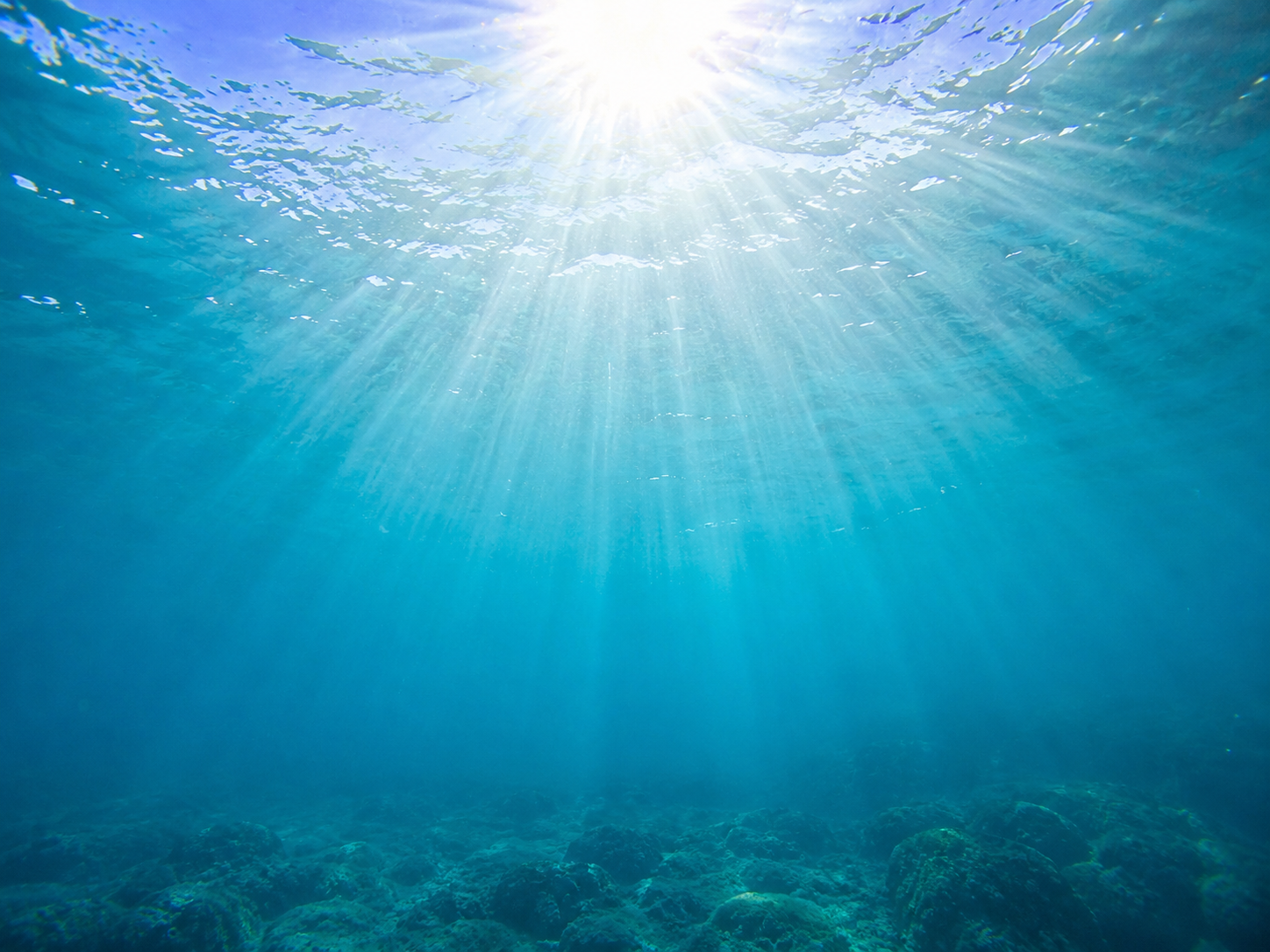 Underwater view looking toward the surface through exceptionally clear turquoise water with sunbeams